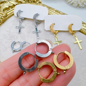 May include: A collection of earrings in silver and gold tones. The earrings include hoop styles and dangle earrings with cross pendants. Some earrings are displayed on white earring cards.