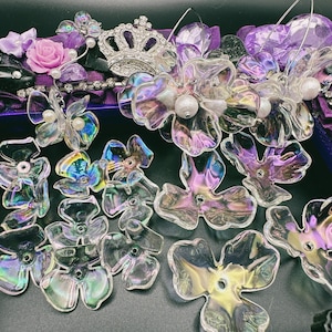 May include: A collection of iridescent glass flower charms in various sizes and shapes. The flowers are clear with a rainbow sheen and have a hole in the center for hanging.