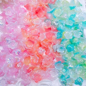 May include: A collection of translucent, flower-shaped beads in shades of pink, orange, and teal. The beads have a glossy finish and are scattered across the image. The beads are likely for crafting or jewelry making.