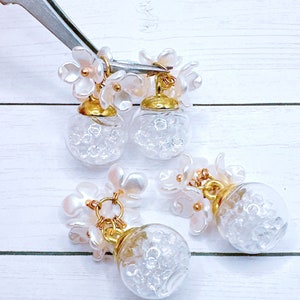 May include: Three pairs of white flower charm earrings with clear glass globe pendants filled with tiny white beads.
