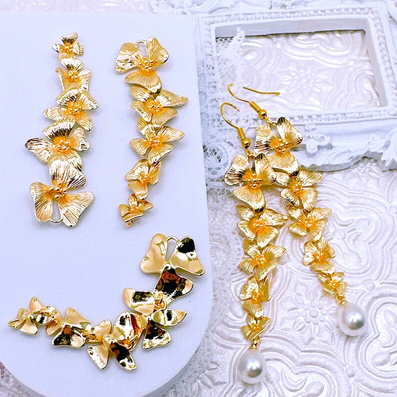 May include: A set of gold-tone earrings featuring a cascade of delicate flower-shaped charms. Each earring is adorned with a single pearl drop.