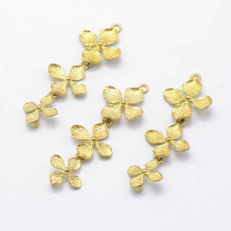 May include: Three gold-toned metal flower charms, each with four petals and a loop at the top. The charms are connected by small chains, creating a cascading effect.
