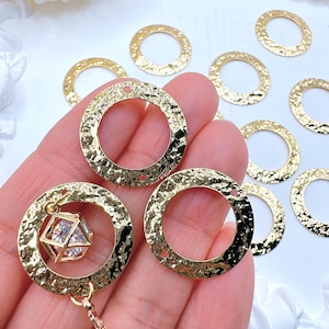 May include: Gold-colored hammered metal jewelry findings. The open circle pendants have a textured surface and a small hole for attaching to other jewelry components. One pendant holds a small, clear, faceted crystal in a gold-colored cage. The findings are for jewelry making.