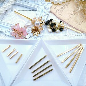 May include: Two white ceramic dishes with gold metal bars arranged in a fan shape. The bars are in two different sizes. The dishes are on a white surface.
