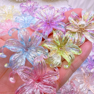 May include: A collection of iridescent, translucent flower-shaped embellishments in various colors, including pink, blue, yellow, and purple. Some flowers have a pearl center and gold chain detail. These decorative elements are ideal for crafts.