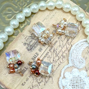 May include: Close-up of four handmade earrings with clear, iridescent crystal cubes and small pearl and bead accents. The earrings are arranged on a vintage paper background with a pearl necklace. The text "BILL OF SALE OF RESED" is visible.