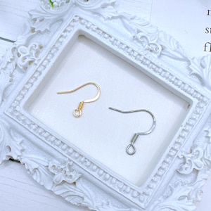 May include: Two earring hooks, one gold and one silver, on a white background. The hooks are made of metal and have a spring closure.