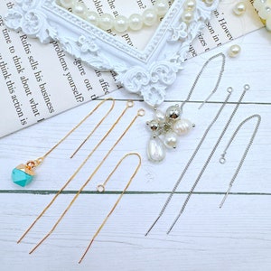 May include: Four pairs of earring findings, two gold and two silver, on a white wooden surface. The findings are made of chain and have a loop at the top. There is a turquoise gemstone pendant on the left side of the image.