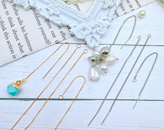 May include: Four pairs of earring findings, two gold and two silver, on a white wooden surface. The findings are made of chain and have a loop at the top. There is a turquoise gemstone pendant on the left side of the image.