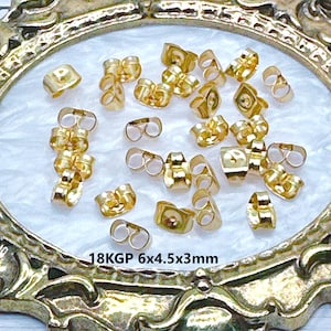 May include: A close-up of a group of 18KGP gold-plated earring backs. The backs are 6mm x 4.5mm x 3mm in size and are arranged on a white surface.