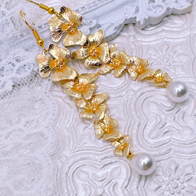 May include: Gold tone earrings with a floral design and pearl accents.