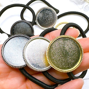 May include: A collection of hair ties with round, metallic bezels in silver, gold, and gunmetal gray. Each bezel is attached to a black elastic band. The bezels have a beaded edge and are designed for crafting or jewelry making.
