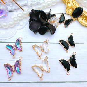 May include: Six butterfly-shaped charms with gold-tone metal accents. Two charms are clear, two are iridescent purple, and two are black.
