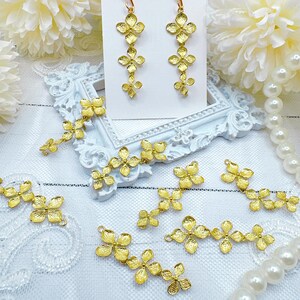 May include: Gold-tone flower-shaped charms arranged in a cluster, with some charms connected in a chain-like pattern. The charms are displayed on a white surface with a white background.