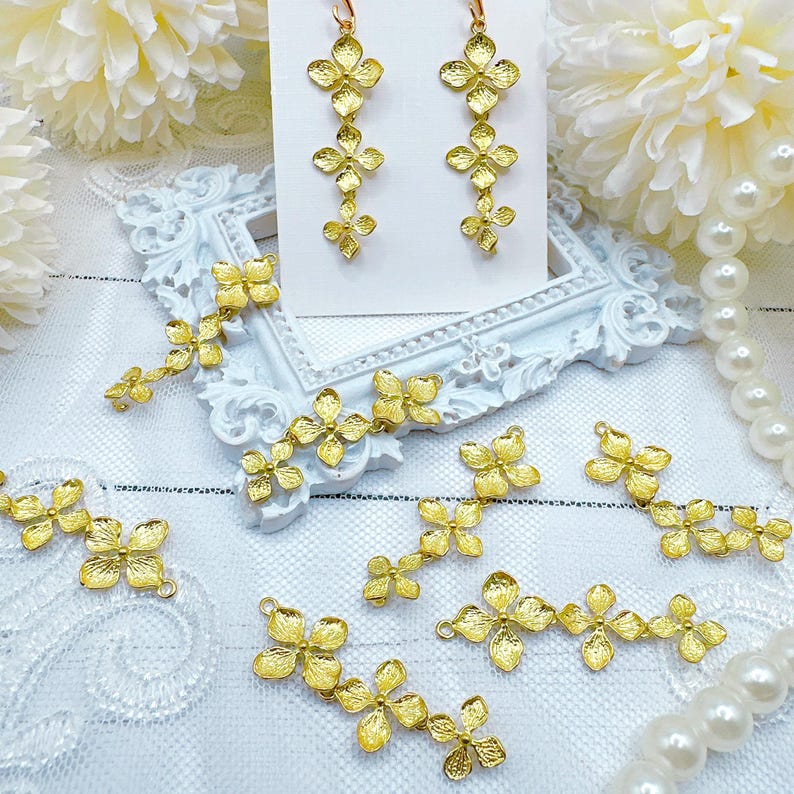 May include: Gold-tone flower-shaped charms arranged in a cluster, with some charms connected in a chain-like pattern. The charms are displayed on a white surface with a white background.