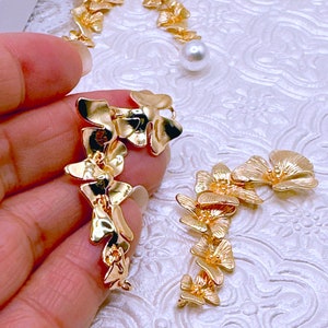 May include: A pair of gold-tone earrings featuring a floral design. The earrings are made of metal and have a delicate, feminine look.