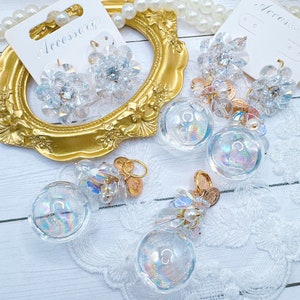 May include: Clear crystal earrings and other jewelry pieces. The earrings are flower-shaped with a central crystal. Other pieces include clear orbs and gold-toned charms. The word "Accessory" is printed on a white tag.