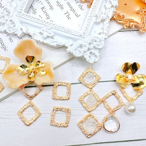 May include: Gold-toned metal earring components with a textured finish. Some of the components are square shaped and some are diamond shaped. There are also clear glass or plastic components and a pearl.