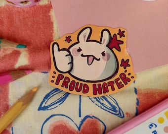 Könnte beinhalten: Ein gelber Aufkleber mit einem Cartoon-Kaninchen, das einen Daumen nach oben zeigt. Der Aufkleber lautet "Proud Hater" in roten und schwarzen Buchstaben.