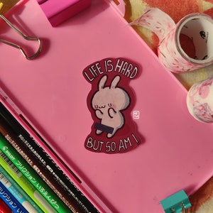 May include: A pink and red sticker with a cartoon bunny and the text "Life is hard but so am I".