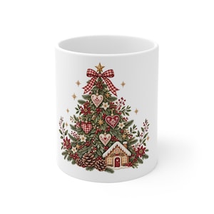 Può includere: Una tazza in ceramica bianca con un'illustrazione festiva di un albero di Natale decorato con ornamenti a forma di cuore rossi e bianchi, un fiocco a quadri rossi in cima, pigne, bacche rosse e una piccola casa di pan di zenzero con stelle.