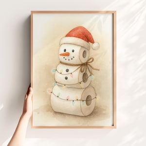 May include: Watercolor print of a snowman made of toilet paper rolls, wearing a red Santa hat and a carrot nose. The snowman is decorated with a string of colorful lights and a brown ribbon. The artwork is framed in a light brown wooden frame.