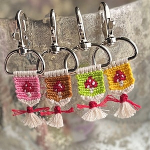 May include: Four colorful mushroom-shaped keychains with tassels. Each keychain is made with a different color of yarn and has a silver metal ring.
