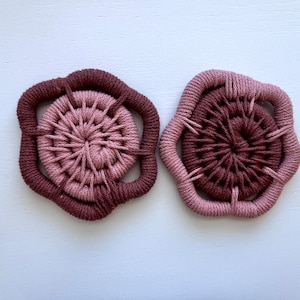May include: Two handmade macrame wall hangings in shades of pink and brown. The hangings are circular with a woven center and a decorative outer edge.