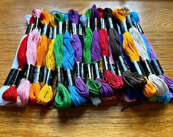Può includere: Una collezione di rocchetti di filo da ricamo colorati, disposti a forma di arcobaleno. I rocchetti sono avvolti in etichette bianche e nere con il nome del marchio.