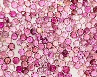 Puede incluir: Una colección de piedras preciosas redondas de color rosa y morado, esparcidas sobre una superficie blanca. Las piedras preciosas son de varios tonos de rosa y morado, algunas tienen un tono más rojizo.