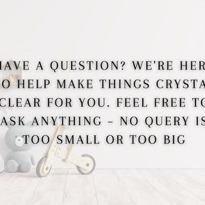 May include: A white wall with black text that reads "HAVE A QUESTION? WE'RE HERE TO HELP MAKE THINGS CRYSTAL CLEAR FOR YOU. FEEL FREE TO ASK ANYTHING - NO QUERY IS TOO SMALL OR TOO BIG". There are toys in the foreground, including a wooden toy scooter, a gray stuffed animal, and a blue stuffed whale.
