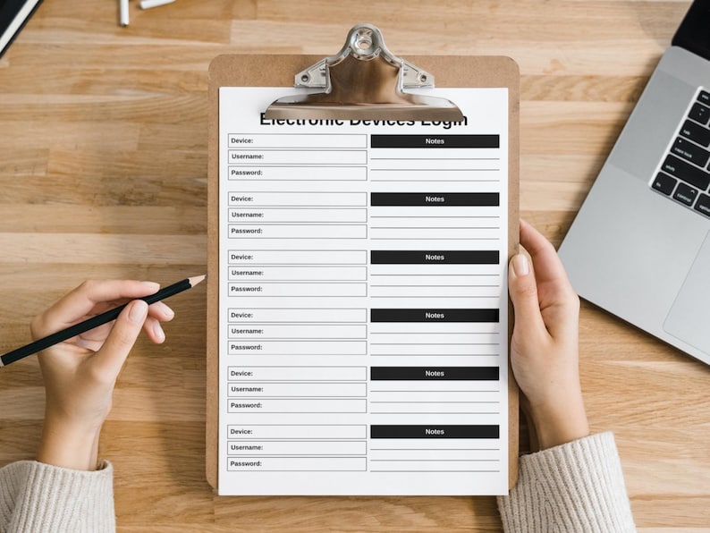 May include: A clipboard with a printed "Electronic Devices Login" form. The form has fields for device, username, password, and notes. A hand holds a pencil, and another hand holds the clipboard. A laptop is visible in the background.