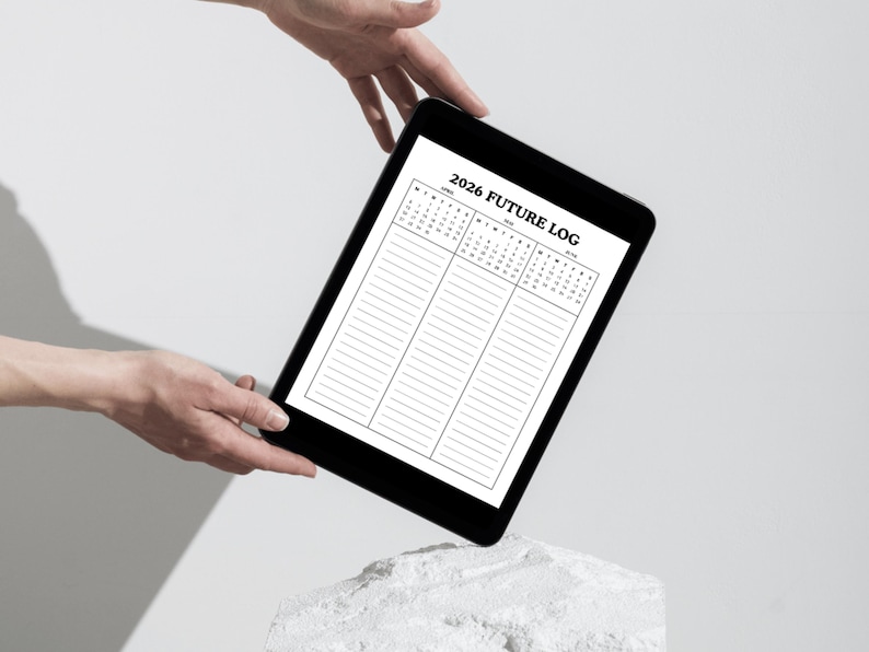 May include: A black tablet displaying a 2026 Future Log calendar with lined sections. The tablet is held by hands against a white background. The calendar layout includes months and dates.