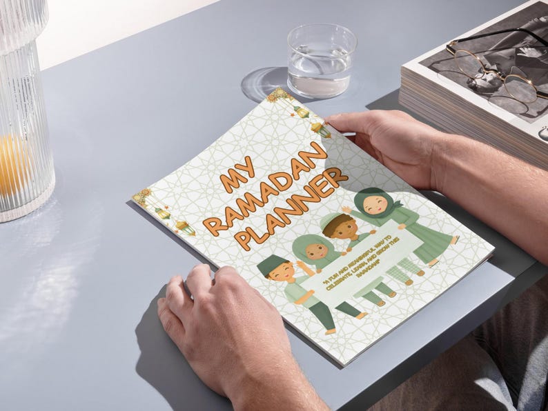 May include: A white and green planner with the text "My Ramadan Planner" in orange. The planner features a colorful illustration of children holding a sign that says "It's fun and meaningful way to celebrate, learn and reflect this Ramadan."