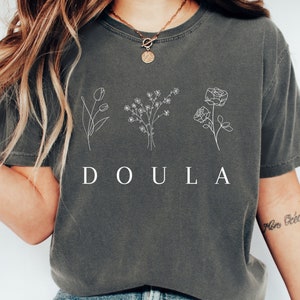 May include: A gray t-shirt with a white graphic of three flowers and the word "DOULA".