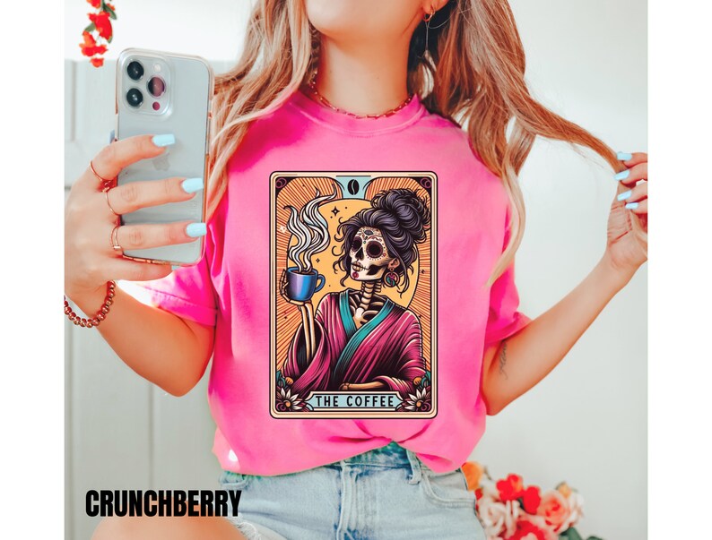 May include: A pink t-shirt with a graphic of a skeleton woman holding a cup of coffee. The graphic is in a tarot card style with the text "The Coffee" at the bottom.
