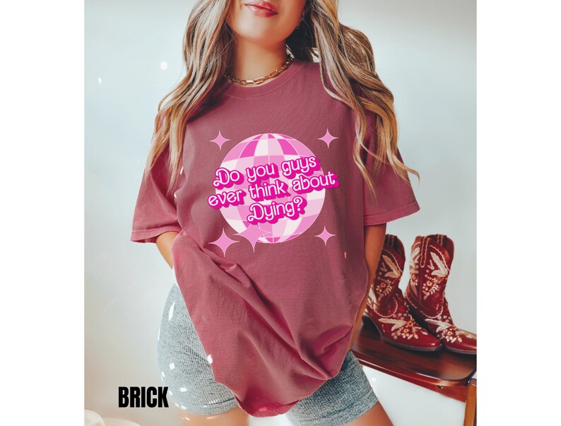 May include: A maroon t-shirt with a pink disco ball graphic and the text "Do you guys ever think about dying?" printed on the front.