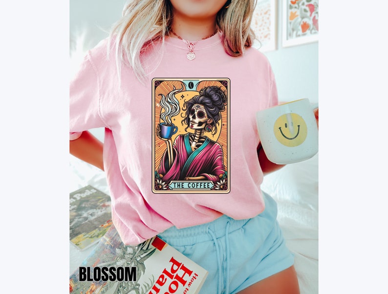 May include: A pink t-shirt with a graphic of a skeleton holding a cup of coffee. The graphic is in a tarot card style with the text "The Coffee" at the bottom.