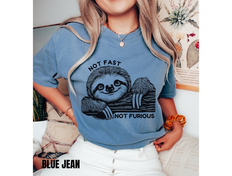 May include: A blue t-shirt with a black graphic of a sloth on a branch. The text "NOT FAST NOT FURIOUS" is printed below the sloth.