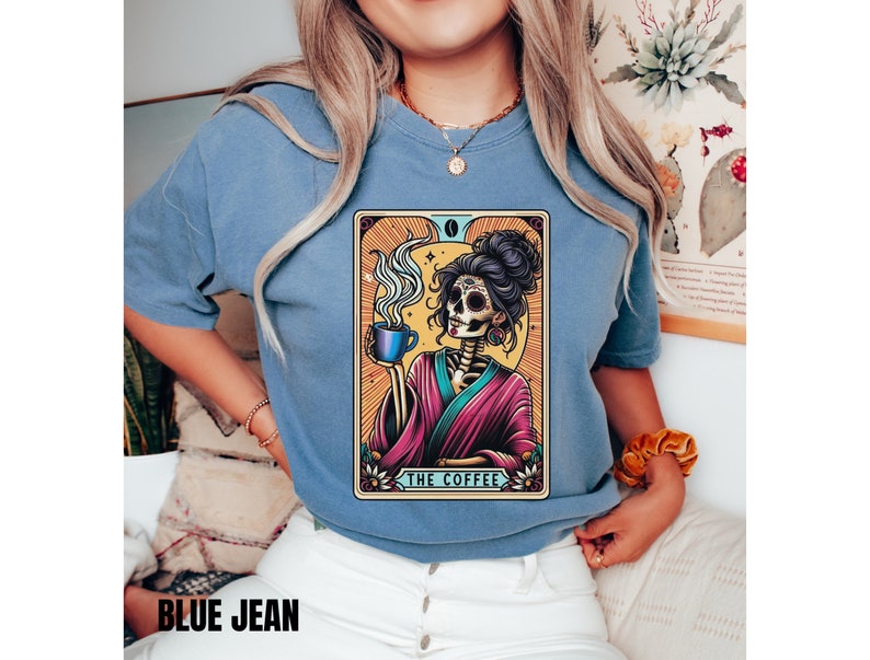 May include: A blue t-shirt with a graphic of a skeleton woman holding a cup of coffee. The graphic is in a tarot card style with the text "The Coffee" at the bottom.