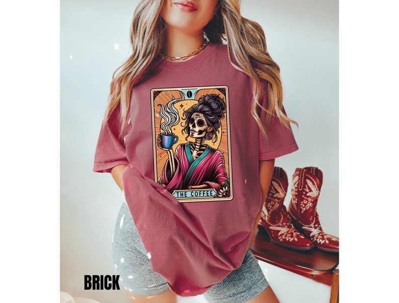 May include: A maroon t-shirt with a graphic of a skeleton woman holding a cup of coffee. The graphic is in a tarot card style with the text "The Coffee" at the bottom.