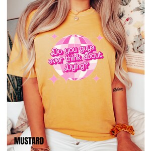 May include: Yellow t-shirt with a pink disco ball graphic and the text "Do you guys ever think about Dying?"