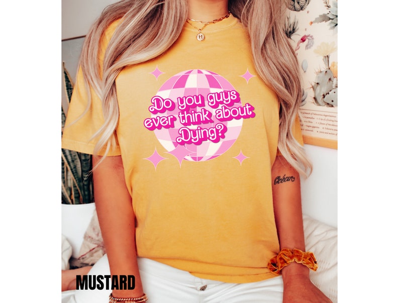 May include: Yellow t-shirt with a pink disco ball graphic and the text "Do you guys ever think about Dying?"