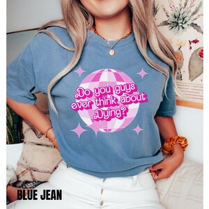 May include: A blue t-shirt with a pink disco ball graphic and the text "Do you guys ever think about Dying?" in pink.