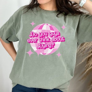 May include: A green t-shirt with a pink disco ball graphic and the text "Do you guys ever think about Dying?" printed on the front.