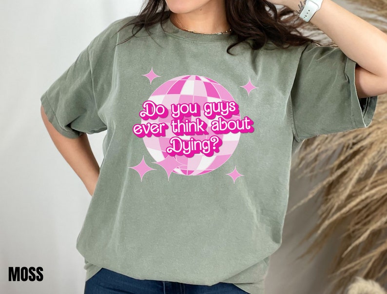 May include: A green t-shirt with a pink disco ball graphic and the text "Do you guys ever think about Dying?" printed on the front.