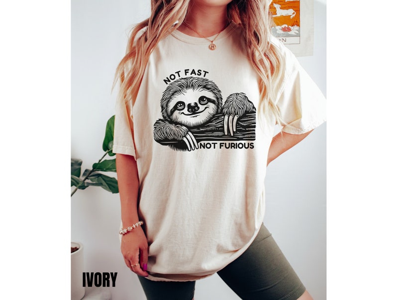 May include: A cream colored t-shirt with a black and white illustration of a sloth hanging from a branch. The text "NOT FAST NOT FURIOUS" is printed on the shirt.