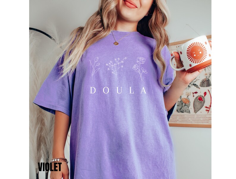 May include: A purple t-shirt with a white graphic of flowers and the word "DOULA" printed on the front.