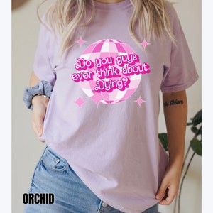May include: A lavender t-shirt with a pink disco ball graphic and the text "Do you guys ever think about Dying?" printed on the front.