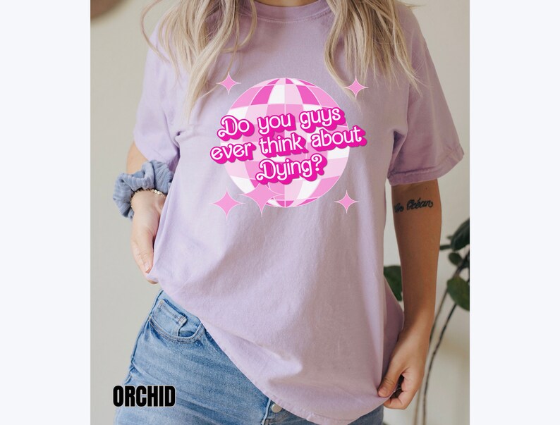 May include: A lavender t-shirt with a pink disco ball graphic and the text "Do you guys ever think about Dying?" printed on the front.